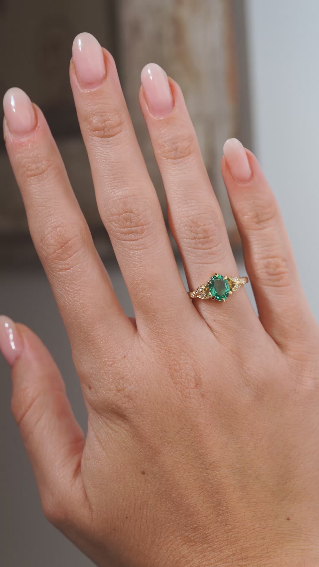 A close-up video of a vintage-inspired emerald and diamond engagement ring modelled on a hand, highlighting the oval green emerald and intricate diamond-set trefoil design.