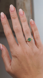 A close-up video of a vintage-inspired emerald and diamond engagement ring modelled on a hand, highlighting the oval green emerald and intricate diamond-set trefoil design.
