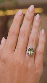 A video of a Vintage, 1950s green beryl and diamond cluster engagement ring worn on a wedding finger and rotated to see the angles and profiles of the ring.  Against a blurred interiors setting. 