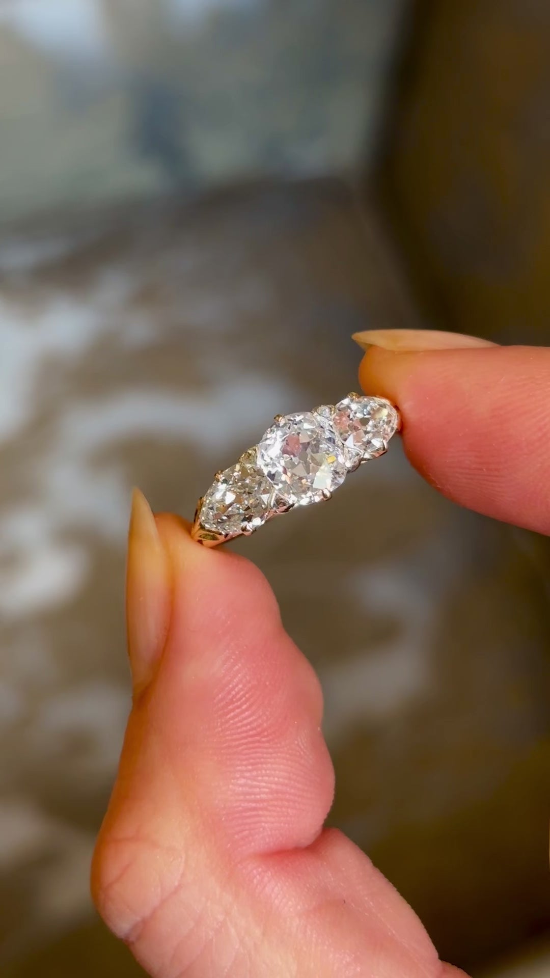 Antique Victorian three-stone with cushion-cut and pear-cut diamonds ring held in fingers and rotated to show details. 