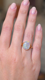 A video of an oval-cut opal set in a yellow gold antique, Edwardian single stone ring worn on the hand and seen from a distance as the hand is slowly moved around.