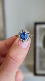 An Antique-inspired, cushion-cut blue sapphire and diamond halo ring in yellow gold shown in the video between fingers.