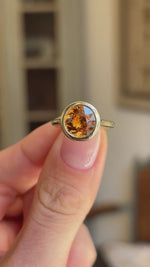 Close up video of an Antique-inspired yellow gold solitaire ring set with an orange zircon in a bezel setting. 