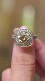 a video of a Vintage, 1990s yellow tinted diamond cluster engagement ring held in the fingers and rotated to show angles