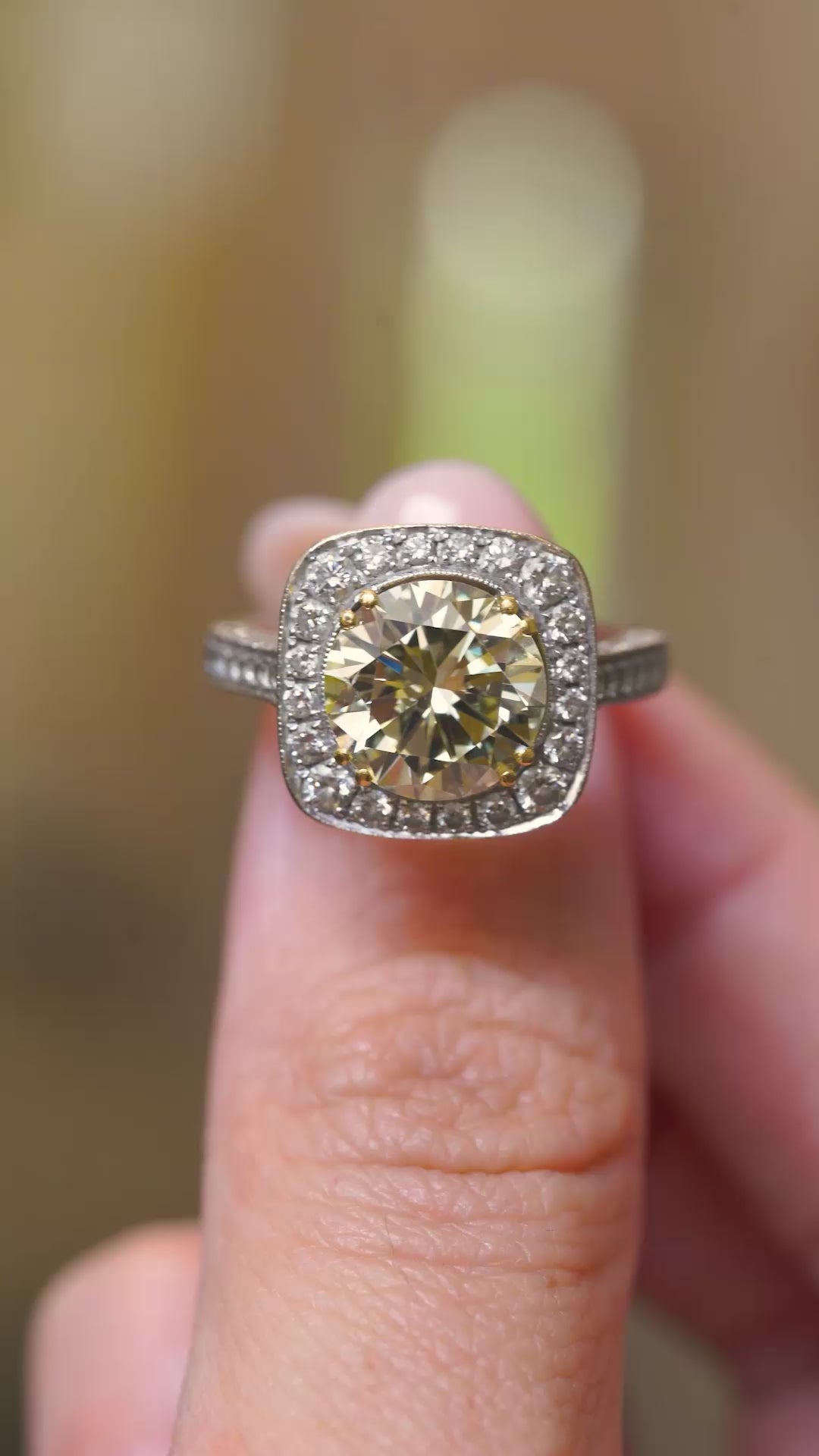 a video of a Vintage, 1990s yellow tinted diamond cluster engagement ring held in the fingers and rotated to show angles