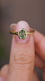 A close up video of an Antique-inspired, Green sapphire solitaire engagement ring, held between two fingers and rotated slowly to showcase the yellow gold bezel setting of the sapphire and band.
