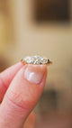 Three stone diamond ring with gold setting details between fingers.