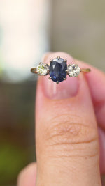 A video of an Antique Art Deco sapphire and diamond trilogy engagement ring in yellow gold held in between the finger and thumb and turned to show off different angles of the ring seen against a blurred background.