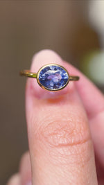 A video of a close detail of an antique-inspired oval-cut blue sapphire solitaire ring in yellow gold held between fingers.