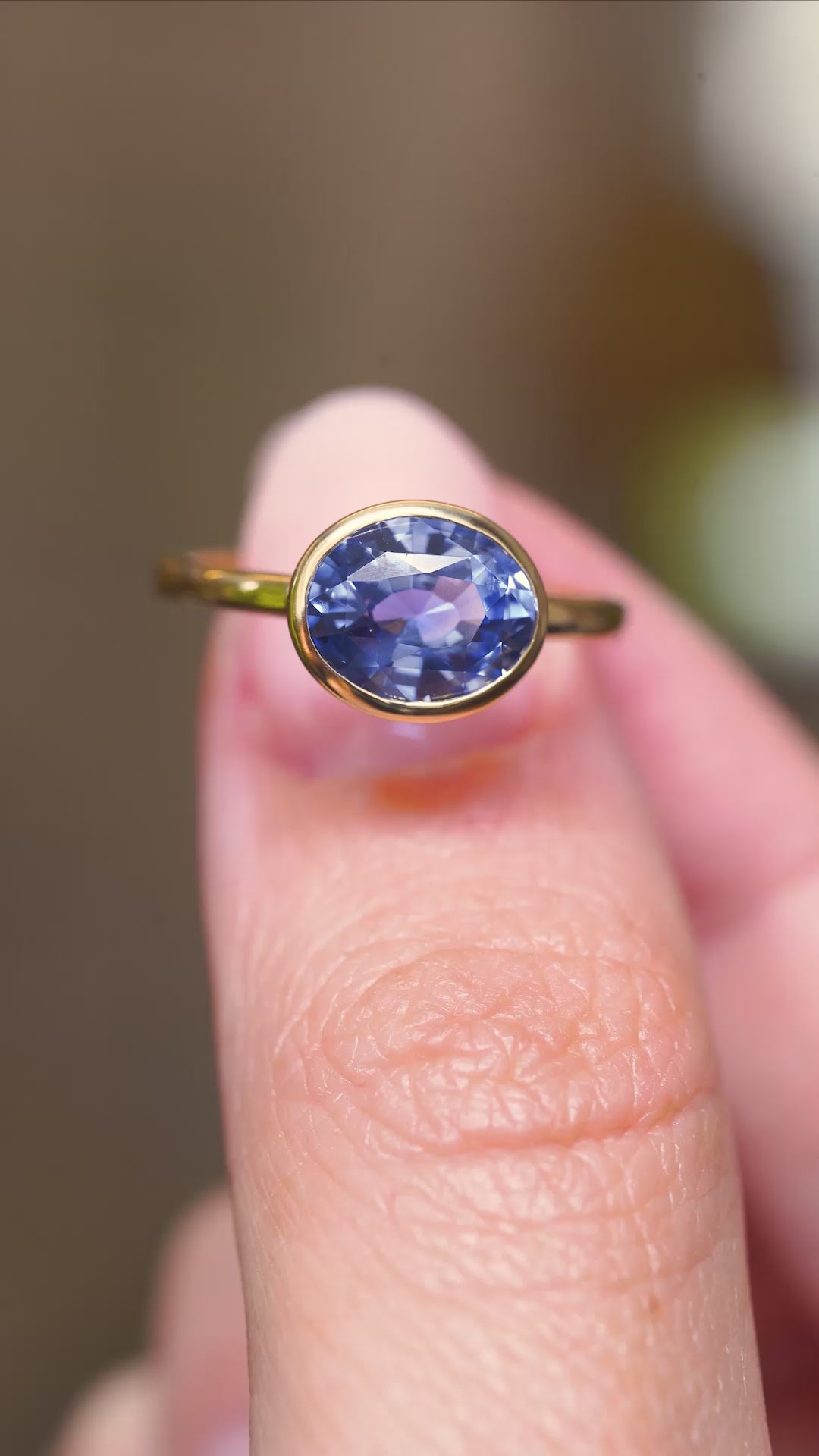 A video of a close detail of an antique-inspired oval-cut blue sapphire solitaire ring in yellow gold held between fingers.