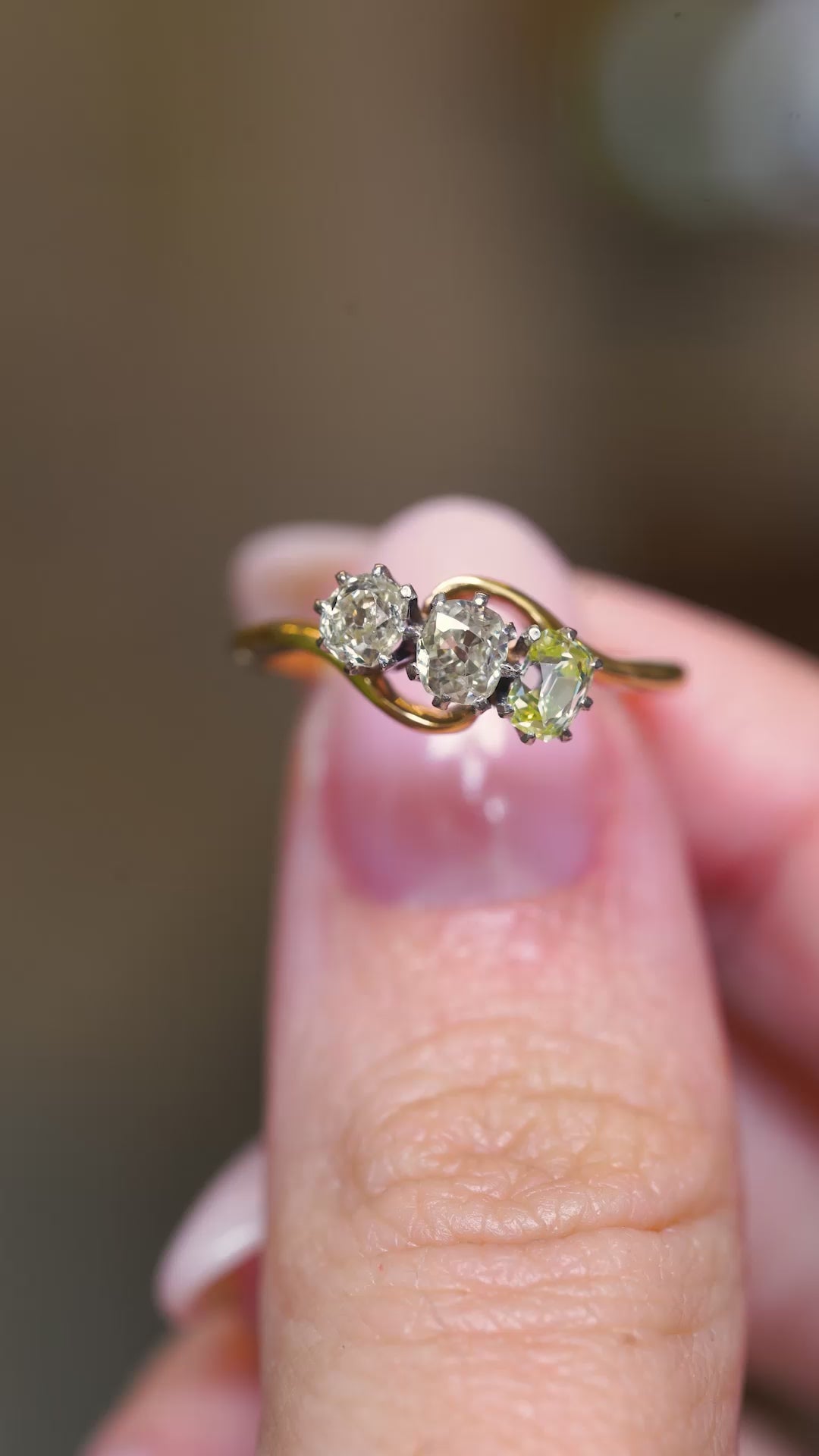 A video of an Art Nouveau three-stone diamond ring held on the finger