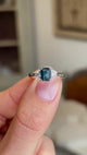 Video of a Vintage-inspired, Teal sapphire and diamond three-stone engagement ring in platinum held between two fingers and rotated to see the full profile of the ring