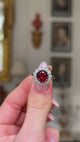 Edwardian garnet and diamond cluster ring, held in fingers and rotated to give perspective.