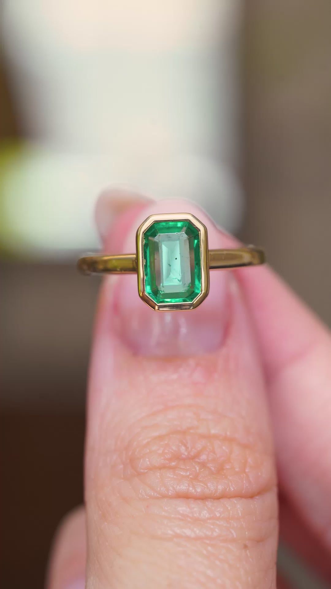 A video of a close-up of an antique-inspired emerald-cut emerald solitaire engagement ring in yellow gold held between fingers.