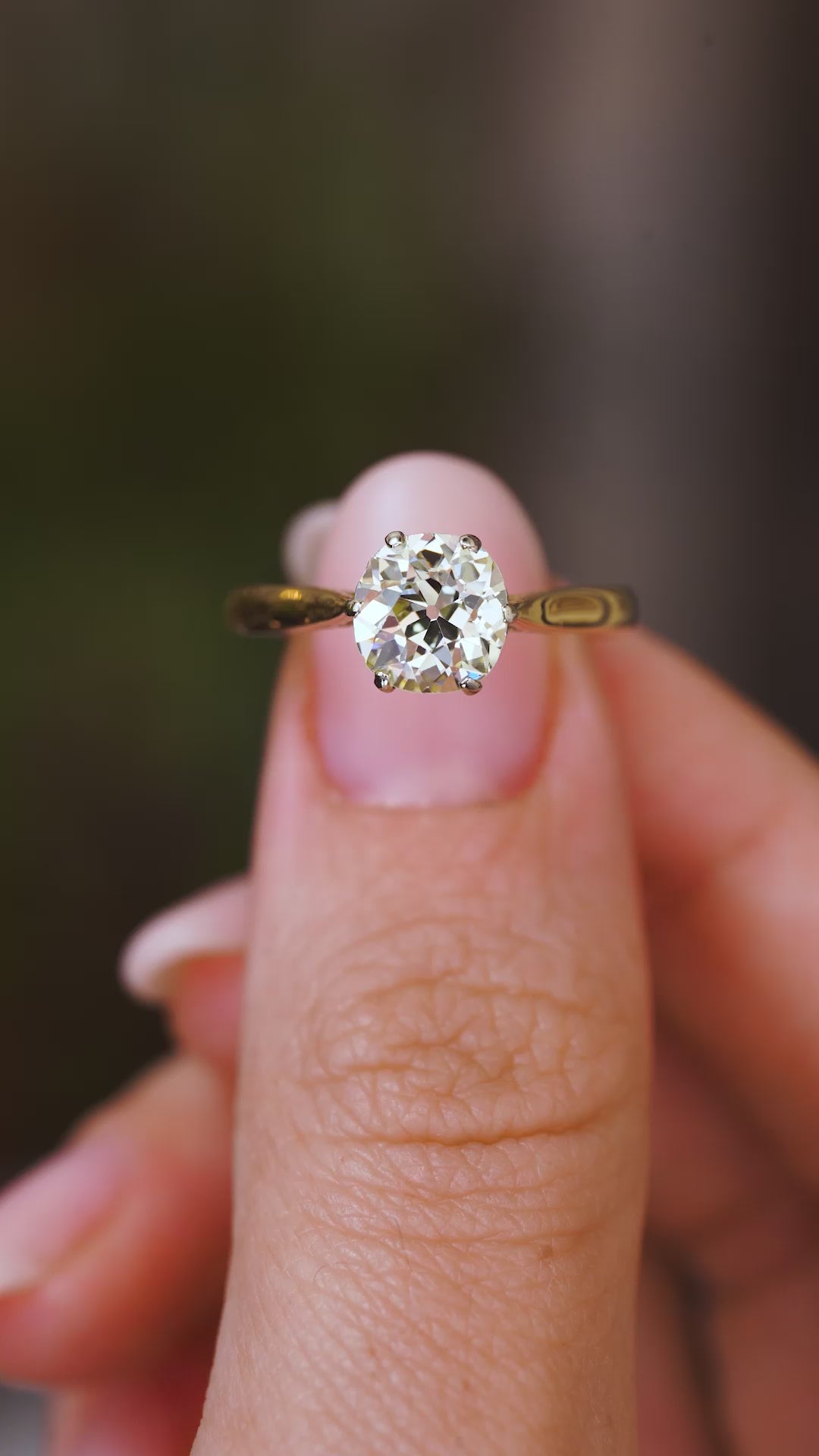 A video of a yellow gold Antique, Edwardian yellow tinted diamond solitaire engagement ring held in fingers and rotated to show different angles