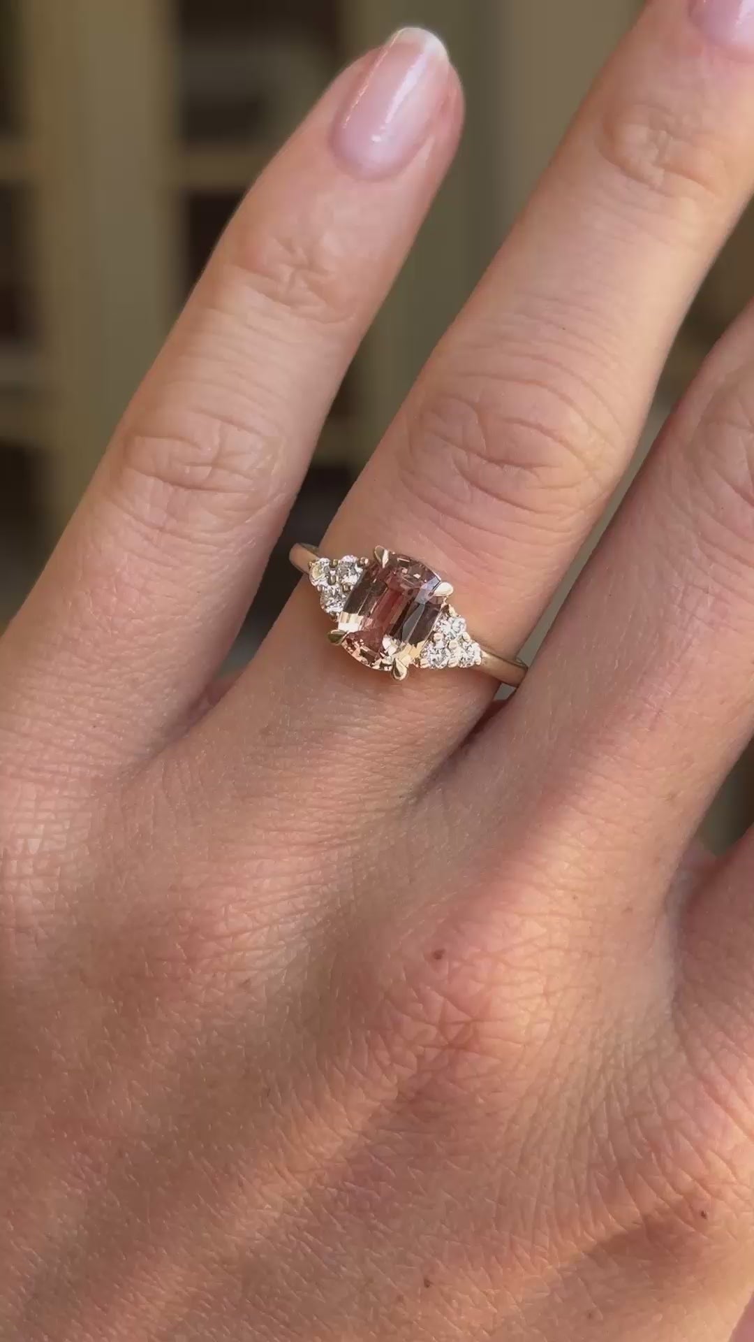 A Vintage-inspired yellow gold engagement ring worn on a person's ring finger, shown in a close-up hand shot with a softly blurred indoor background.