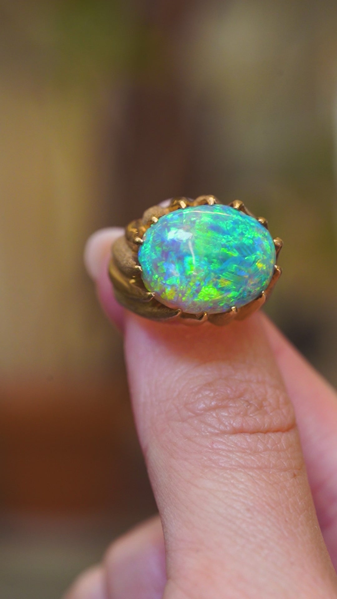 A close-up video of a vintage cabochon Australian opal ring in 18ct yellow gold shown between fingers.