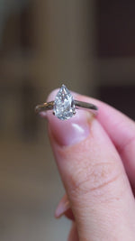 Vintage salt and pepper diamond solitaire ring held between fingers showing pear-shaped diamond detail in slow motion.