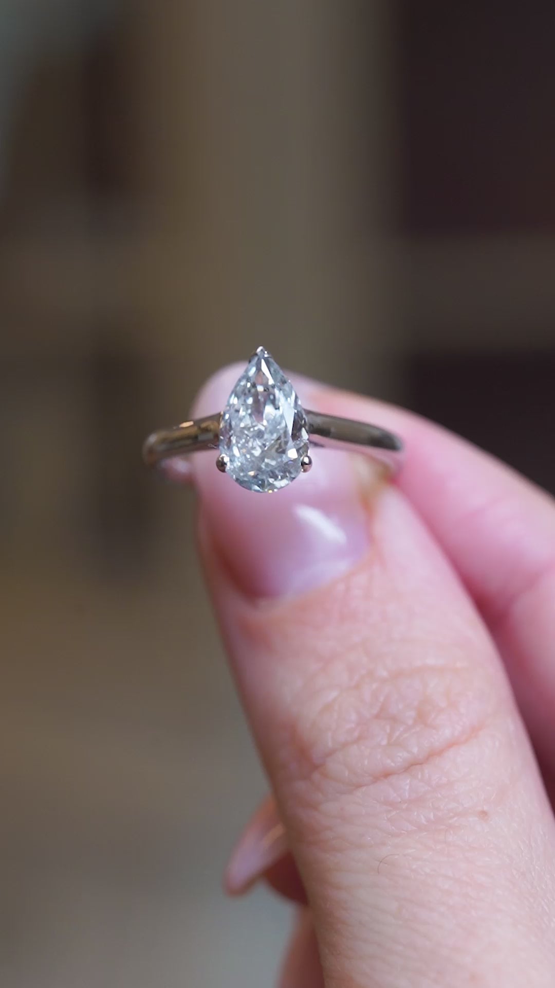 Vintage salt and pepper diamond solitaire ring held between fingers showing pear-shaped diamond detail in slow motion.
