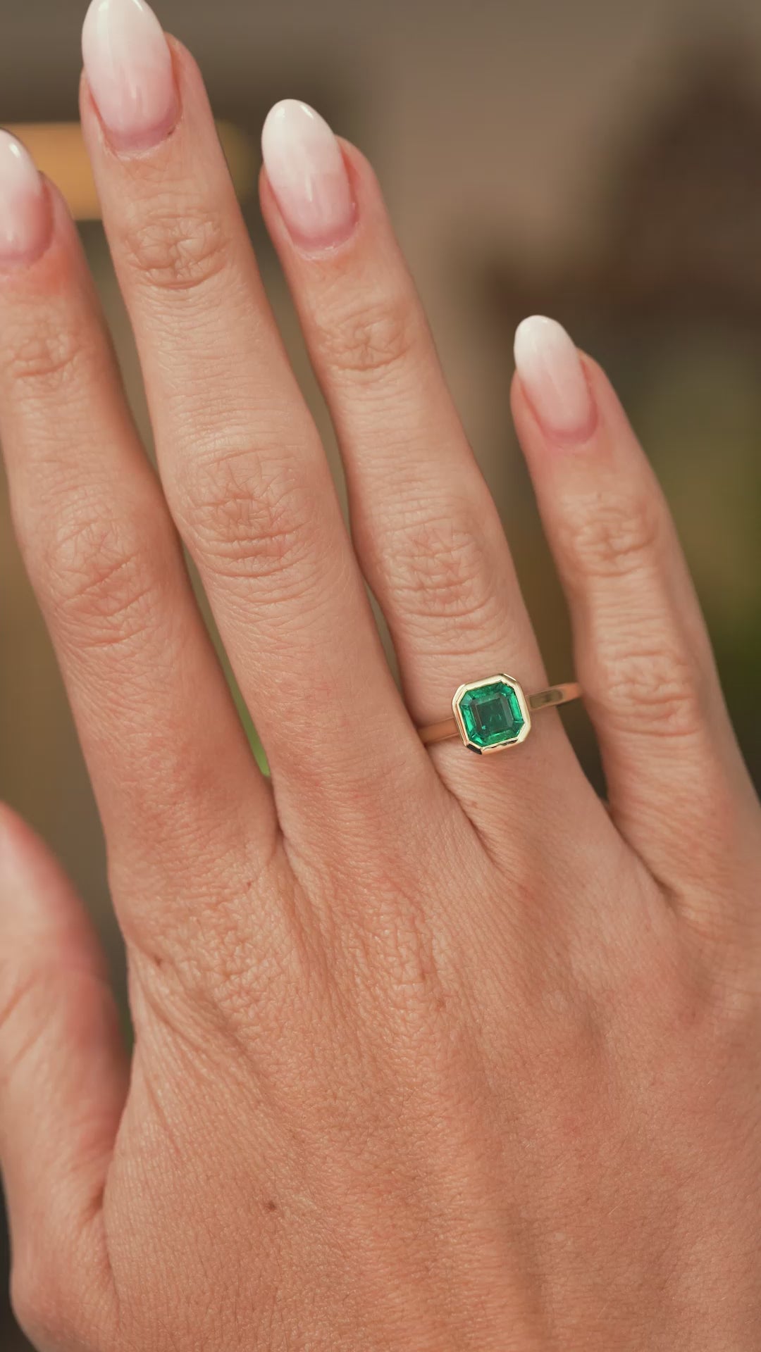 A video of a hand wearing a yellow gold Antique-inspired, Emerald solitaire engagement ring and showing off the scale.