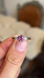 Pink-red sapphire and diamond three-stone engagement ring showcasing a vibrant pink-red sapphire flanked by pear-cut diamonds, held by hand to highlight the setting and craftsmanship.