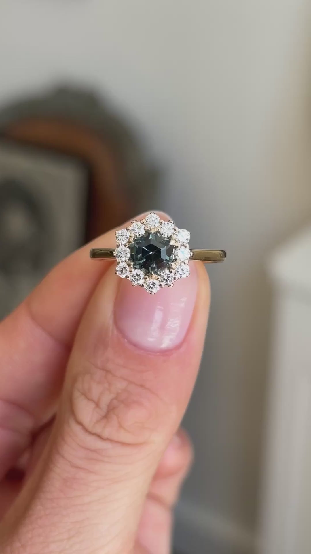 Teal hexagon-cut sapphire and diamond cluster engagement ring featuring a hexagon-cut teal sapphire surrounded by brilliant-cut diamonds, held by hand to showcase the setting and gallery.