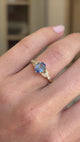 Blue sapphire and diamond engagement ring featuring an oval blue sapphire centre stone with diamond-set trefoil shoulders in the form of laurel leaves, displayed on a hand.