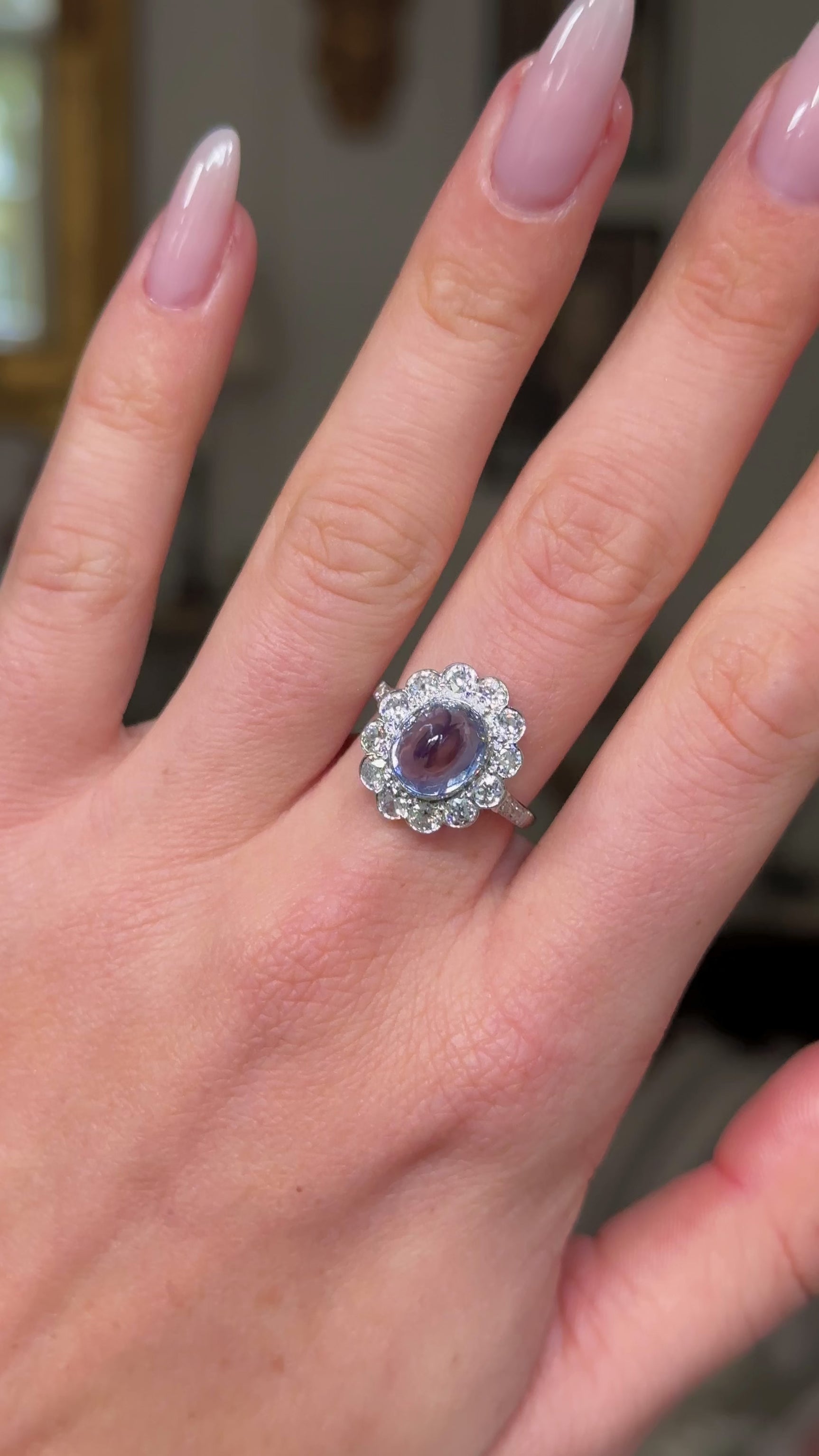 cabochon sapphire and diamond cluster ring set in platinum worn on hand and moved away from camera to give perspective. 