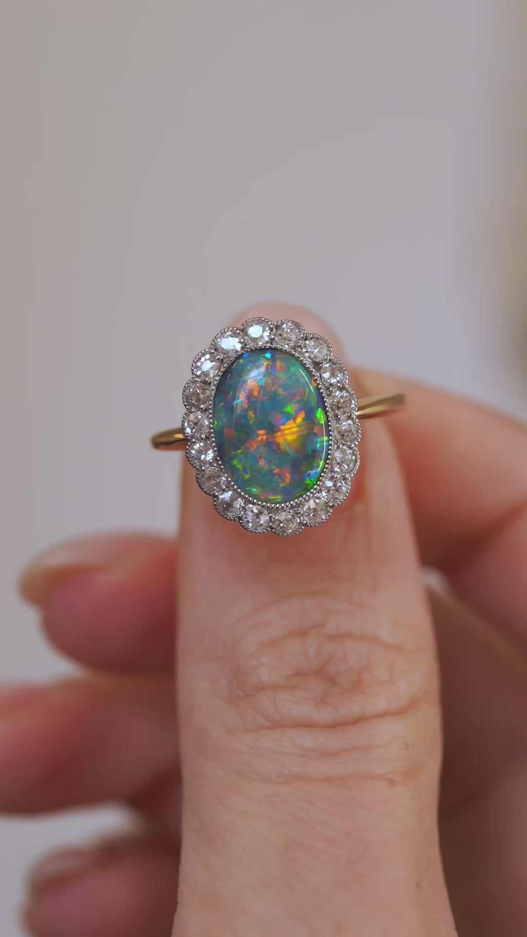 Video presenting the antique opal ring balanced on a fingertip for a clear view of its colourful centre and diamond border.