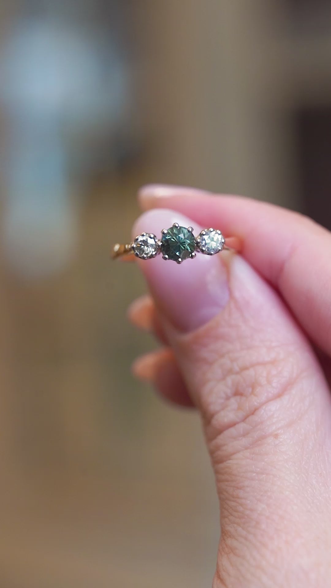 Close detail video of vintage 1950s green sapphire and diamond three-stone engagement ring shown between fingers.