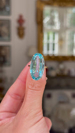 aquamarine and yellow gold cocktail ring held in left hand. Shot with hand up close rotating the ring to give a full perspective,  antiquated bokeh background. 