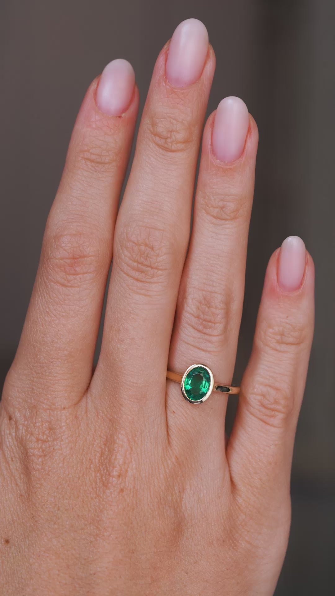 A video of an Antique-inspired, Emerald solitaire engagement ring being worn on a wedding finger, rotated slowly to show the profile of the setting once worn on the hand and the yellow gold band. 