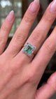 square-cut emerald and diamond cluster ring, worn on hand and moved away from lens to give perspective, front view.