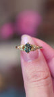 Pine green sapphire and diamond engagement ring held between fingers showing ring details.