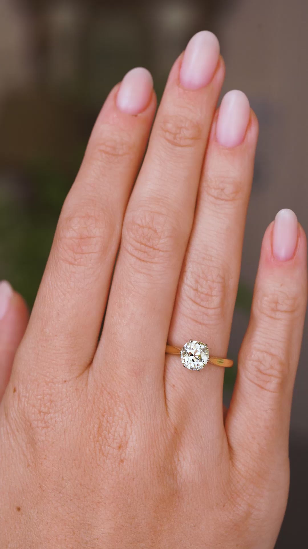 A video of an Antique, Edwardian yellow tinted diamond solitaire yellow gold engagement ring worn on a hand as it slowly turns.