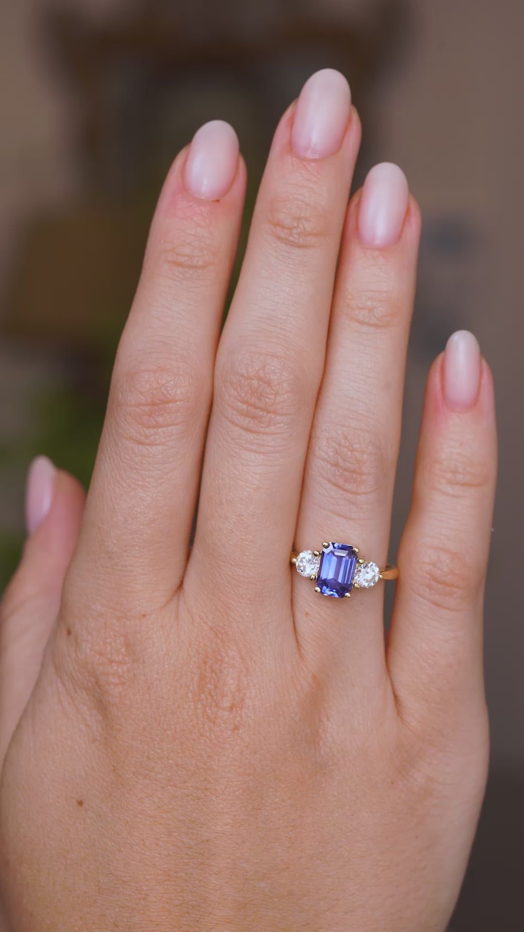 Video of a hand wearing a Vintage inspired three-stone yellow gold engagement ring, worn on a wedding finger and rotated slowly to showcase the central Sri Lankan blue sapphire and two flanking round-cut diamonds.  