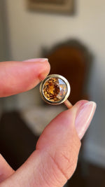 Close up video of an Antique-inspired, Deep orange zircon solitaire ring in yellow gold with a rub-over setting.  Held between two fingers and rotated slowly to view all angles.