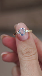 A video of the oval blue sapphire ring held on a fingertip, showcasing a detailed view of the three stones and yellow gold engagement ring. 