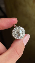 Detailed video of a vintage 1950s platinum diamond cluster engagement ring, held between fingers to showcase the substantial diamond cluster, exceptional fire and elegant mid-century design against a warm interior setting.
