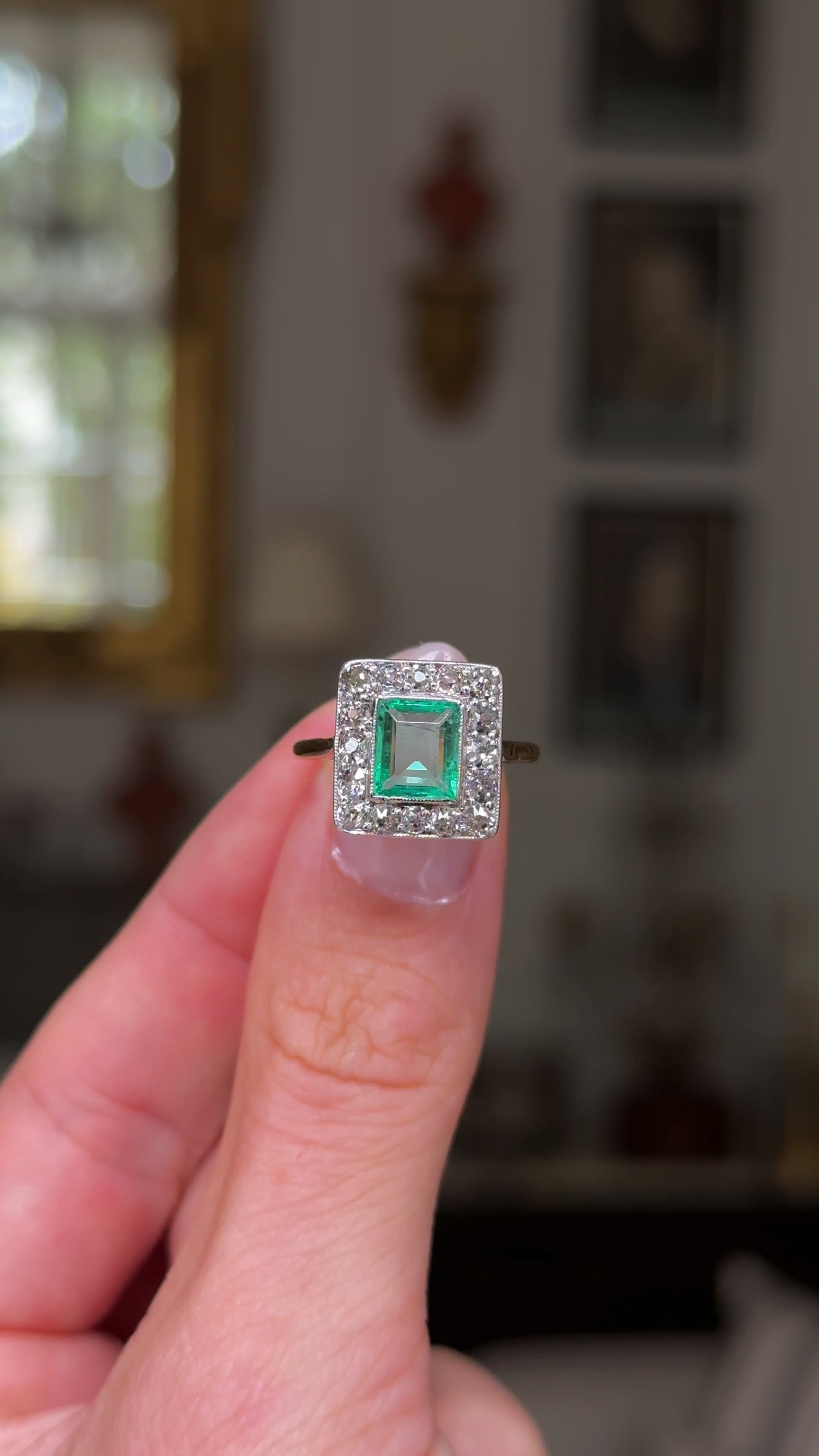 square-cut emerald and diamond cluster ring,  held in fingers and rotated to give perspective, front view.