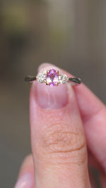 A video of a Vintage, 1990s pink sapphire and diamond three-stone engagement ring in platinum held in between the fingers and turned to show off different angles of the ring.