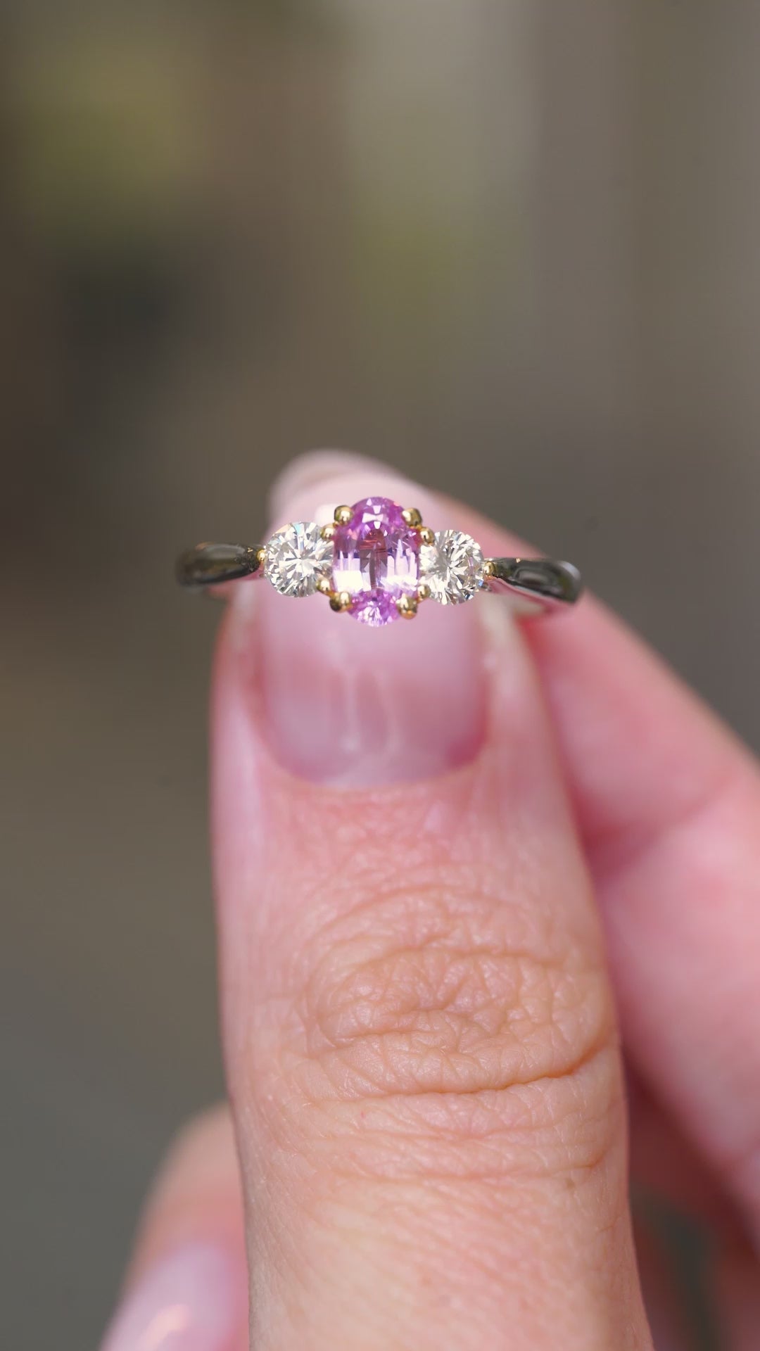 A video of a Vintage, 1990s pink sapphire and diamond three-stone engagement ring in platinum held in between the fingers and turned to show off different angles of the ring.