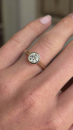 Vintage inspired diamond rub-over solitaire engagement ring featuring a round brilliant-cut diamond in a rub-over setting, displayed on a hand.