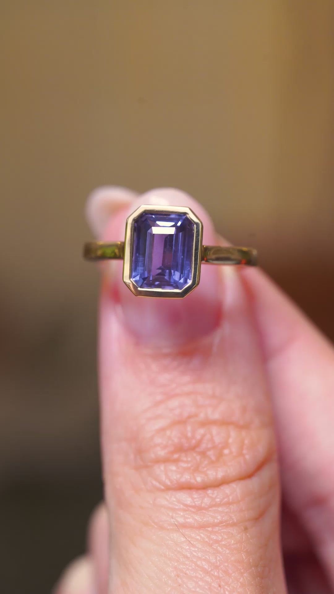 A video of a close-up of an antique-inspired indigo blue sapphire solitaire ring with a yellow gold band held between two fingers.