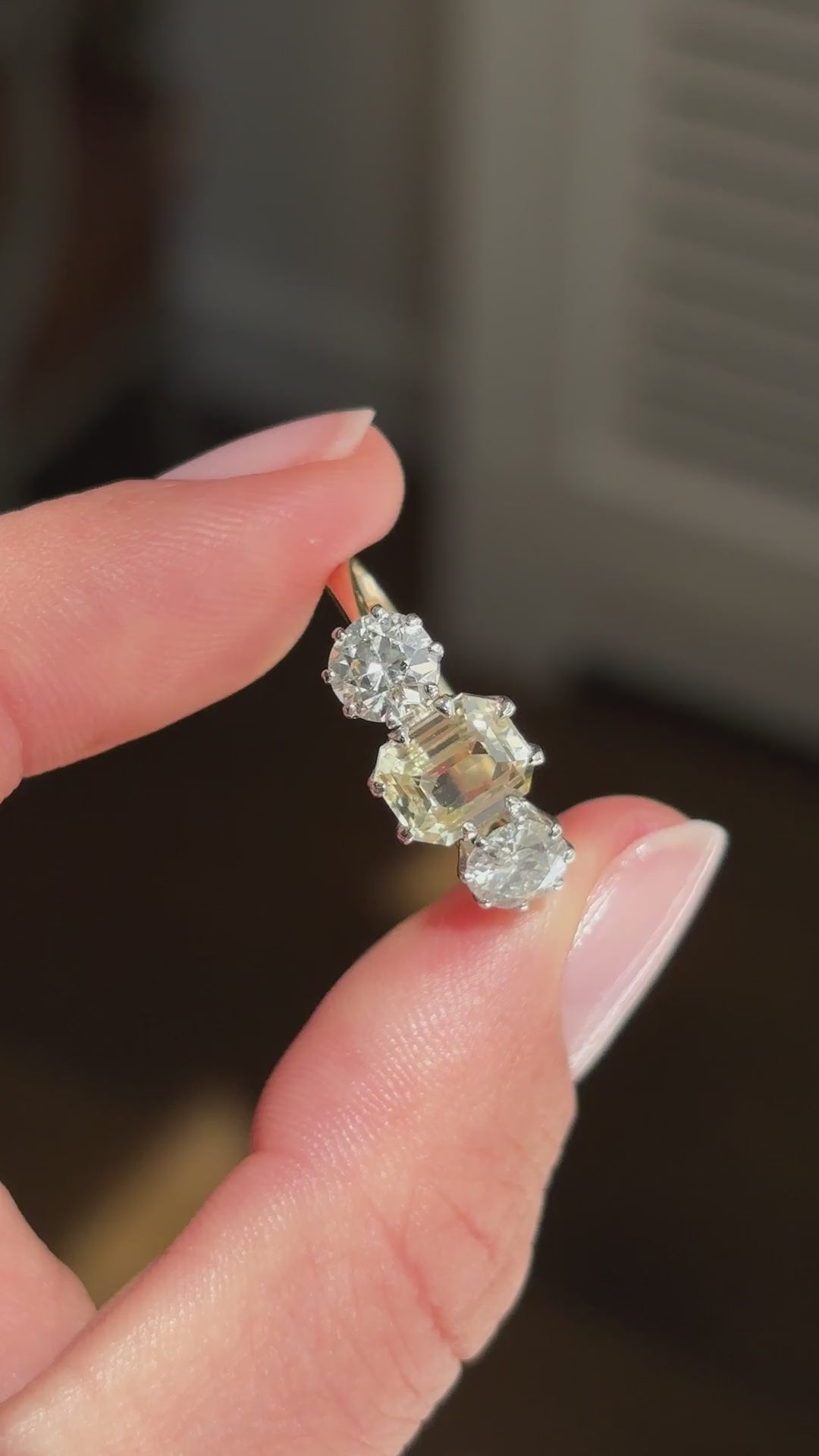 Vintage 1970s yellow sapphire and old-cut diamond three-stone engagement ring featuring an emerald-cut yellow sapphire and old-cut diamond side stones, held by hand for detailed viewing.