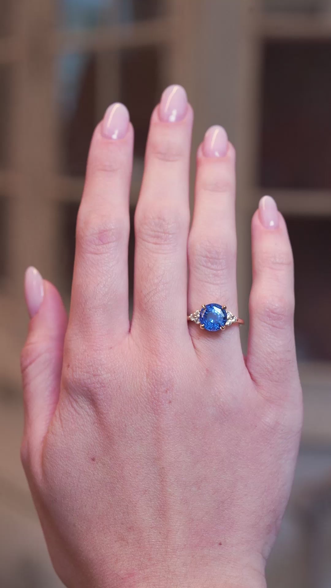 Round blue sapphire and diamond cluster tre-foil engagement ring worn on hand shown in slow motion.