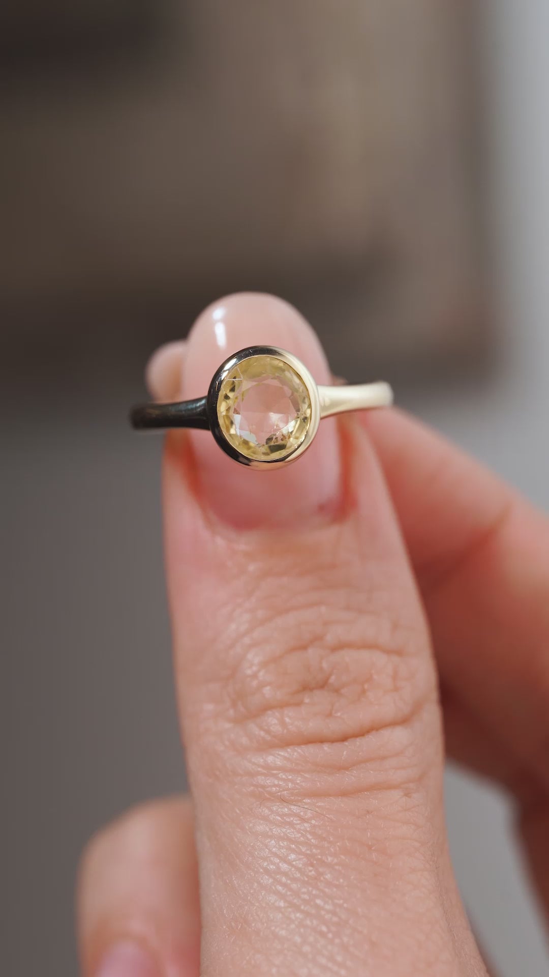 A close-up video of an antique-inspired pale yellow sapphire solitaire engagement ring held between fingers, displaying the gemstone's subtle golden reflections and smooth yellow gold bezel setting.