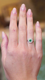 Antique Edwardian emerald and old-mine cut diamond cluster ring shown in movement on a hand.