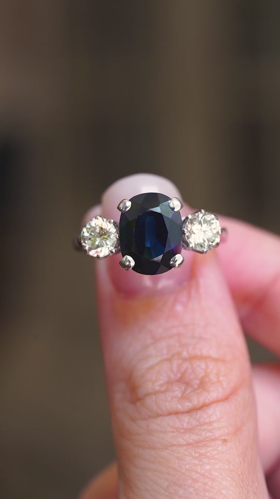 A vintage, 1970's midnight-blue sapphire and diamond three-stone ring in white gold shown in video between fingers.