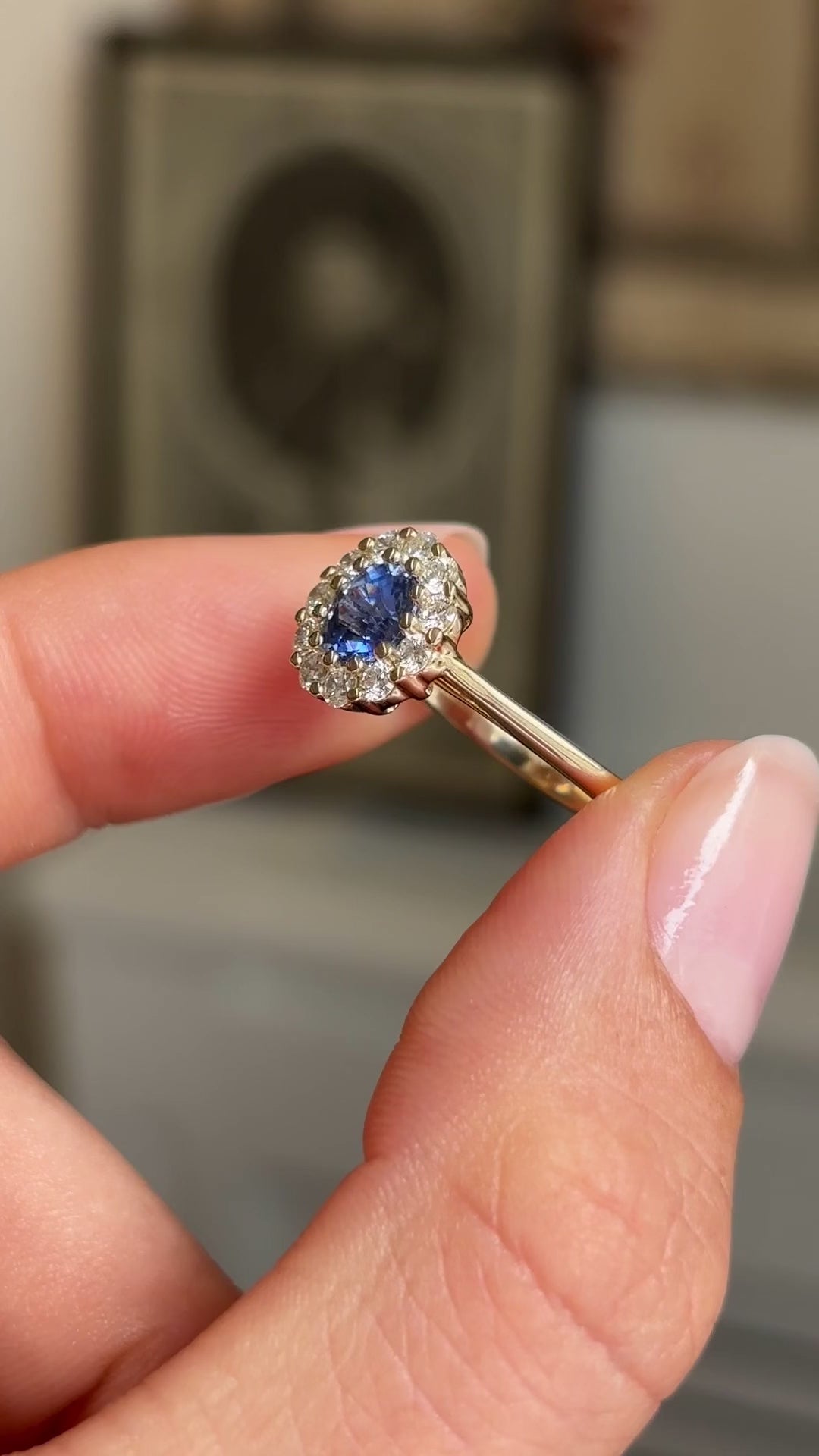 Video of an Antique-inspired,  blue sapphire and diamond cluster engagement ring in yellow gold, held between two fingers and rotated to display all angles of the ring. 